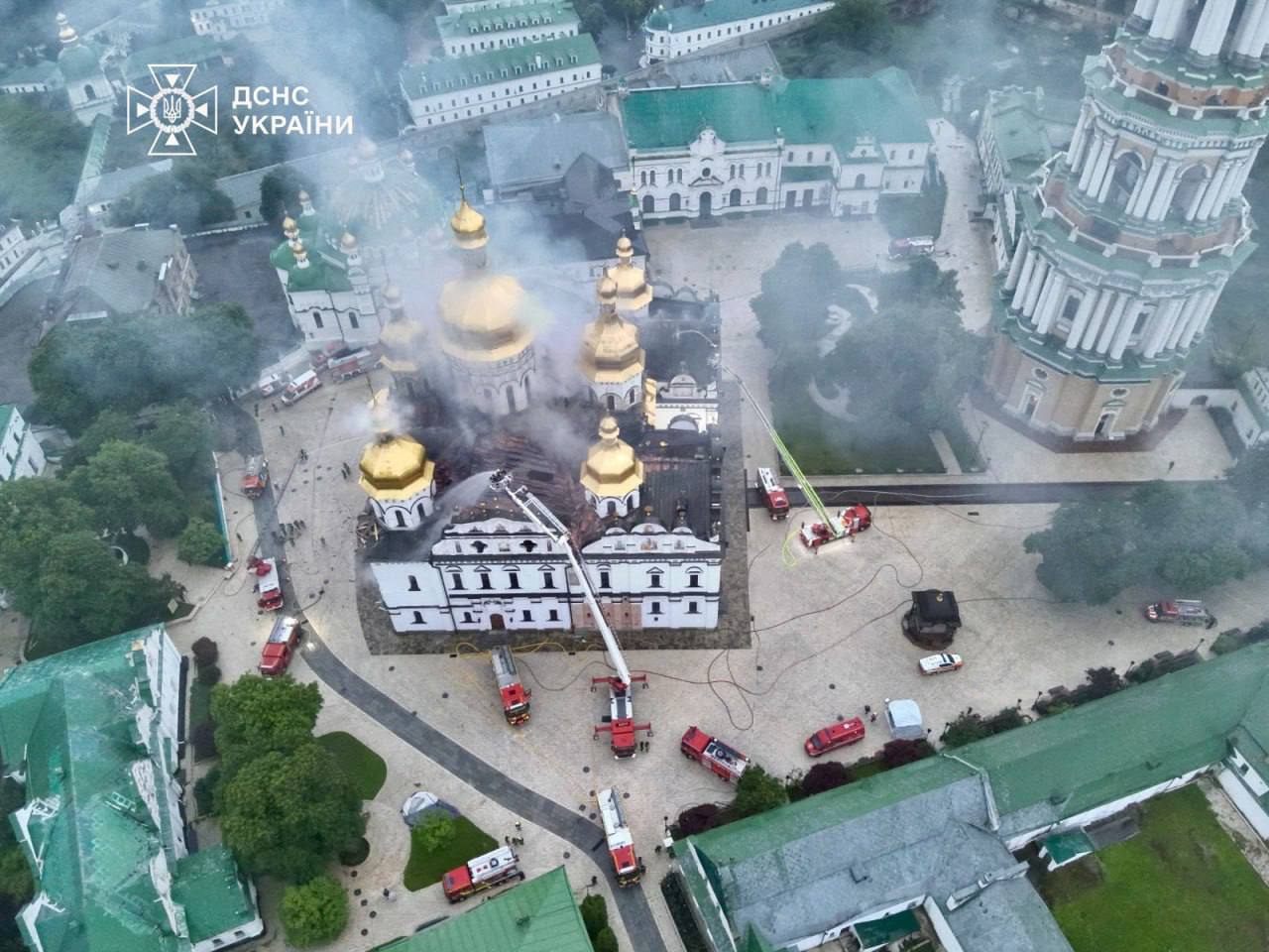 High aerial overview of the Dormition Cathedral and Kyiv-Pechersk Lavra with smoke rising and many fire engines and aerial ladders deployed around it, 15 June 2026.